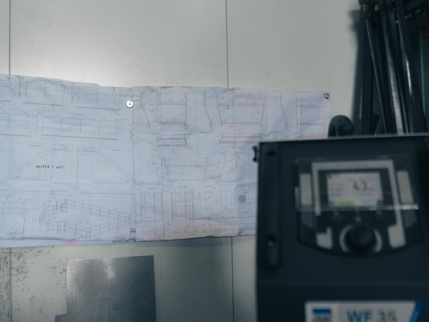 Plan d'exécution punaisé au mur, près d'un poste de travail.